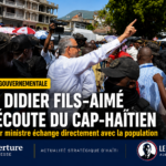 Le Premier ministre Alix Didier Fils-Aimé serre des mains et salue la foule rassemblée dans une rue animée du Cap-Haïtien, entouré de gardes du corps et de citoyens souriants.